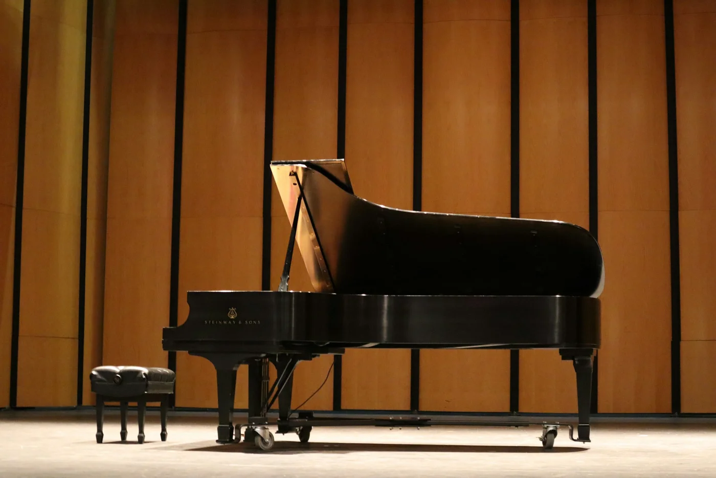 Grand piano hitam dengan tutup terbuka di depan panel kayu